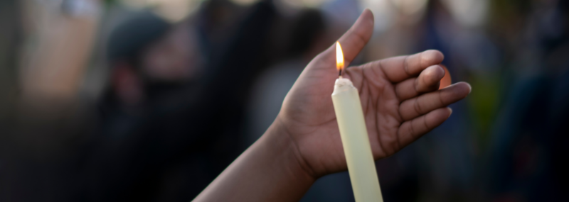 Relief from Gun Violence; pictured is a hand holding a lit candle in rememberance of their loved one.
