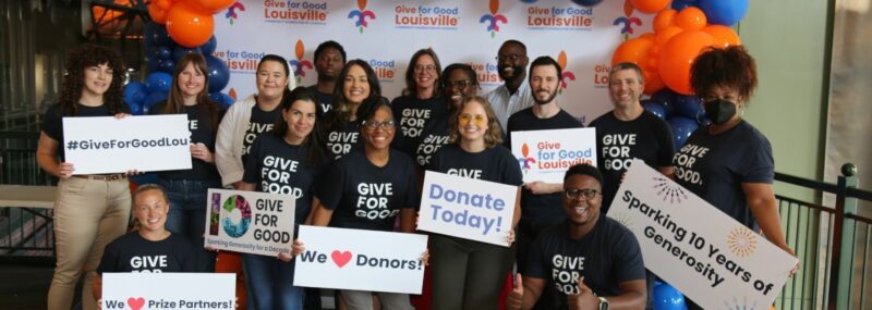 Group of people smiling, posing with signs that read Give for Good Louisville
